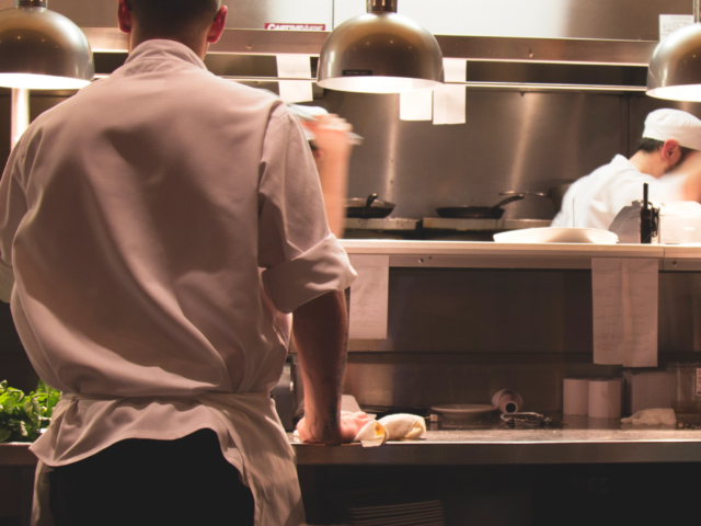 The image displays two chefs at work at a countertop in a kitchen. They appear to be preparing meals and are dressed sturdily. Most likely, the kitchen is located in a restaurant. Additionally, details on new overtime laws that will help workers starting in July 2024 are provided.(Source: rawpixel)