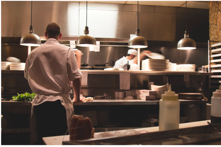 The image displays two chefs at work at a countertop in a kitchen. They appear to be preparing meals and are dressed sturdily. Most likely, the kitchen is located in a restaurant. Additionally, details on new overtime laws that will help workers starting in July 2024 are provided.(Source: rawpixel)