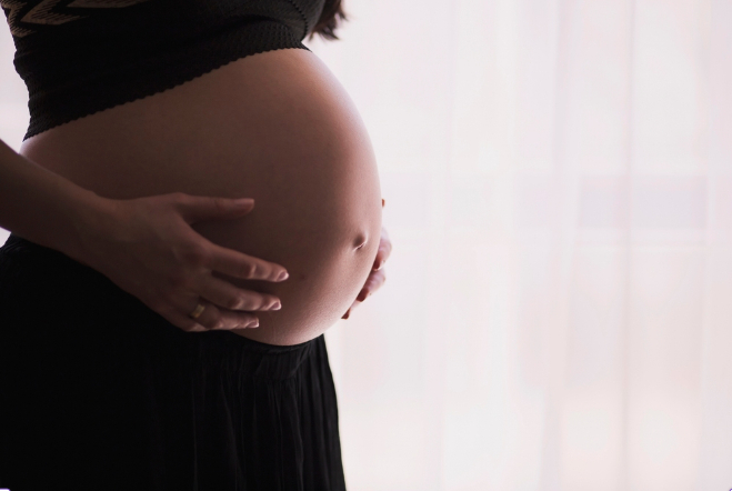 Pregnant woman in black holds her exposed stomach expectantly. Photo Source: RawPixel {CC0 1.0 DEED}