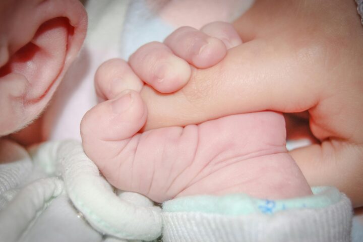 Crop sleeping newborn baby grasping parents finger