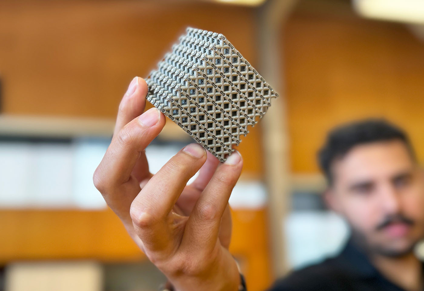 PhD candidate Jordan Noronha holding a sample of the new titanium lattice structure 3D printed in cube form.