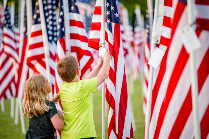 Children read a dedication card on a flag at the Field of Honor at Greenville Town Common, Greenville. Photo Source: Rawpixel (CC0 1.0)