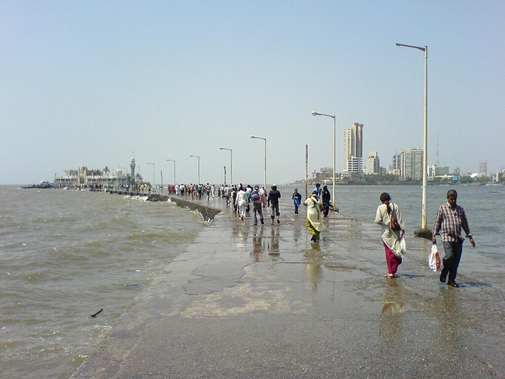 The Haji Ali Causeway, People walking out to Haji Ali Dargah along the causeway. Mumbai skyline in the background. Photot Source: Rakesh Krishna Kumar (Flicker)