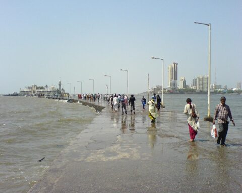 The Haji Ali Causeway, People walking out to Haji Ali Dargah along the causeway. Mumbai skyline in the background. Photot Source: Rakesh Krishna Kumar (Flicker)