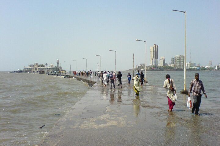 The Haji Ali Causeway, People walking out to Haji Ali Dargah along the causeway. Mumbai skyline in the background. Photot Source: Rakesh Krishna Kumar (Flicker)