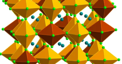 Structure of the gold-halide perovskite. The elongated gold-chloride octahedra, composed of gold (Au) surrounded by six neighboring chlorine (Cl) atoms, are shaded in the structure: burnt-red octahedra represent Au2+-chloride and gold octahedra represent Au3+-chloride. Turquoise spheres represent cesium (Cs) atoms, and light- green spheres represent chlorine (Cl) atoms. The inset shows the shortest gold-chloride bonds. Image credit Karunadasa et al. 2023.