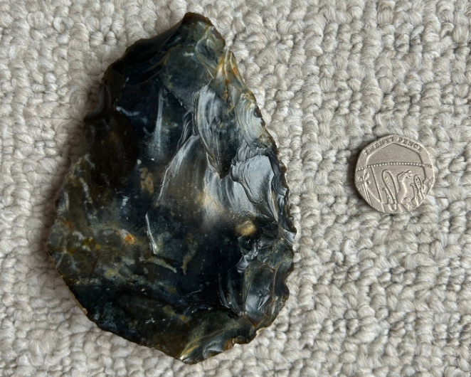 A hand axe discovered at Shoreham Beach, shown beside a 20 pence coin for scale comparison.