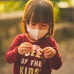 Representative Image. A little girl wearing face mask looking at the flower she is holding. Photo Source: ANNGO Ng (Pexels)