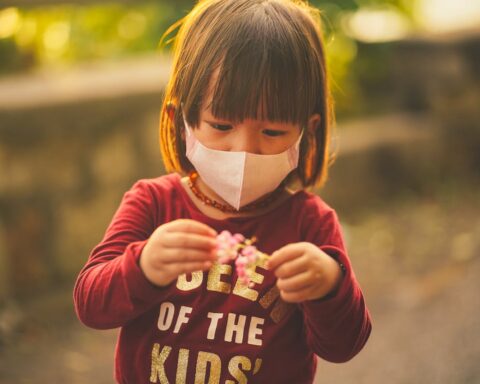 Representative Image. A little girl wearing face mask looking at the flower she is holding. Photo Source: ANNGO Ng (Pexels)