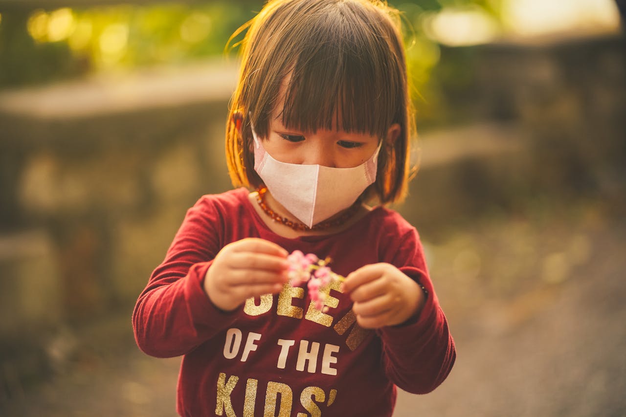 Representative Image. A little girl wearing face mask looking at the flower she is holding. Photo Source: ANNGO Ng (Pexels)