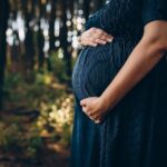 Representative Image. Pregnant woman embracing belly while standing in forest. Photo Source: Helena Lopes (Pexels)