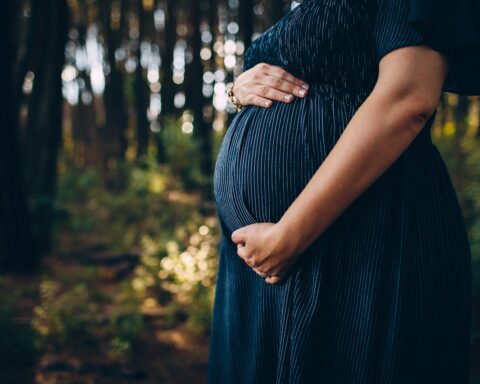 Representative Image. Pregnant woman embracing belly while standing in forest. Photo Source: Helena Lopes (Pexels)