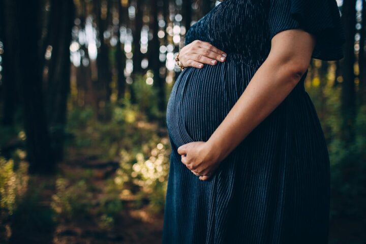 Representative Image. Pregnant woman embracing belly while standing in forest. Photo Source: Helena Lopes (Pexels)