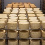 Cheese wheels are neatly arranged on racks in a well-lit storage room.