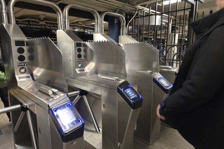 A man stands beside a metal machine in a New York subway station, surrounded by urban transit elements.