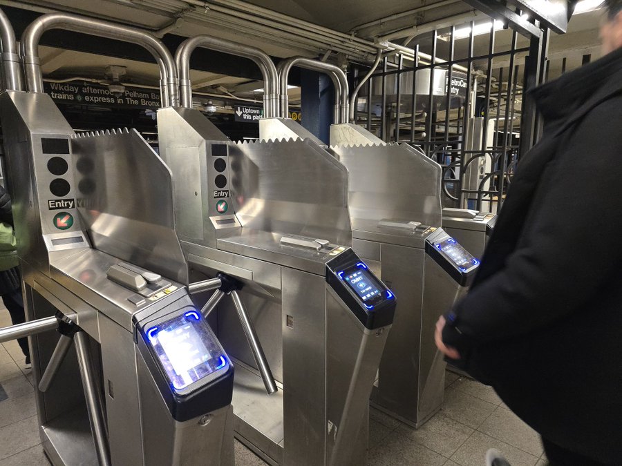 A man stands beside a metal machine in a New York subway station, surrounded by urban transit elements.