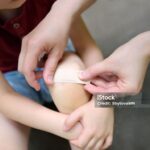 Representative Image. Mother hands applying antibacterial medical adhesive bandage on child's knee after falling down. First aid for kids after injury/trauma. Photo Source: SbytovaMN (IStock)