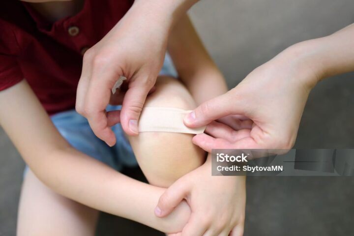 Representative Image. Mother hands applying antibacterial medical adhesive bandage on child's knee after falling down. First aid for kids after injury/trauma. Photo Source: SbytovaMN (IStock)