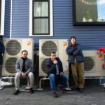 Five people pose beside outdoor heat pump units. Photo Source: Nancy W. Stauffer | MIT Energy Initiative.