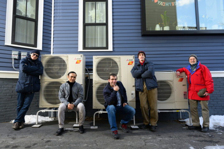 Five people pose beside outdoor heat pump units. Photo Source: Nancy W. Stauffer | MIT Energy Initiative.