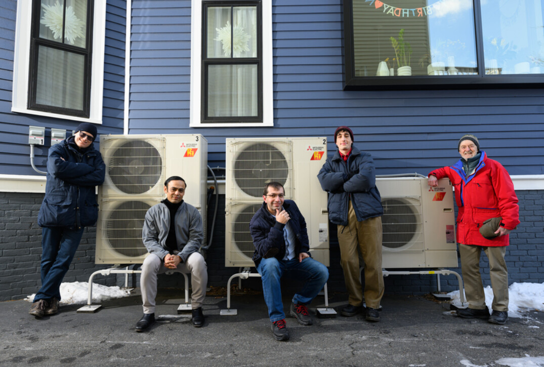 Five people pose beside outdoor heat pump units. Photo Source: Nancy W. Stauffer | MIT Energy Initiative.