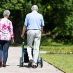 Representative Image: Two People Walking in a Park. Elderly couple walking along a pathway in a park or garden. The man is using a walker for support, while the woman walks beside him. Photo Source: Rollz International (Pexels)