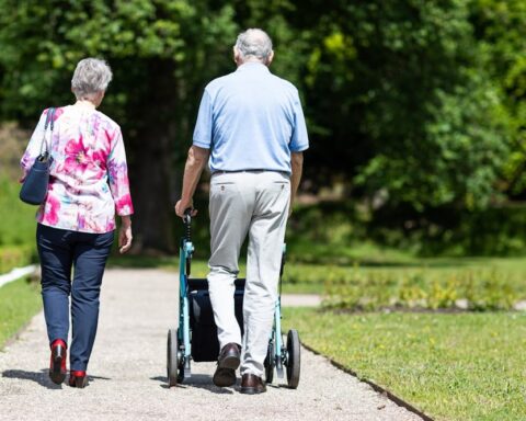 Representative Image: Two People Walking in a Park. Elderly couple walking along a pathway in a park or garden. The man is using a walker for support, while the woman walks beside him. Photo Source: Rollz International (Pexels)