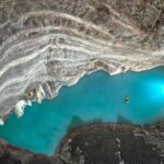 Two kayakers explore a glowing blue pool in a vast, rocky cave. Photo Source: Nadace Neuron