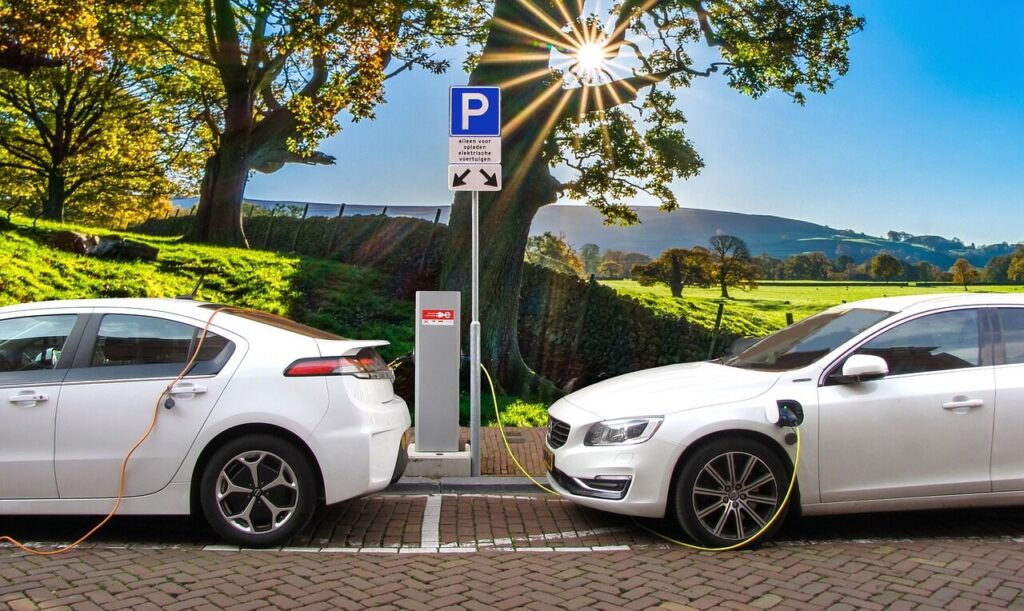 Representative image. Two white electric cars charge at a station under a bright sun and blue sky. Photo Source: Joenomias.