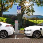 Representative image. Two white electric cars charge at a station under a bright sun and blue sky. Photo Source: Joenomias.