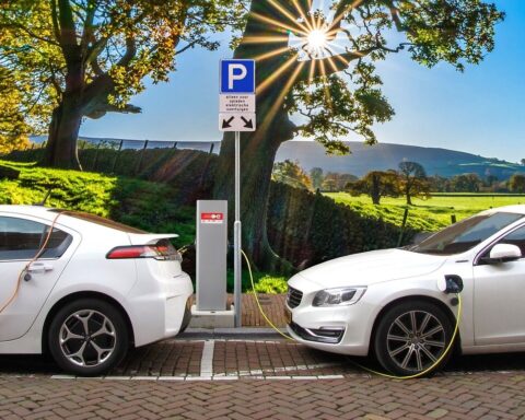 Representative image. Two white electric cars charge at a station under a bright sun and blue sky. Photo Source: Joenomias.