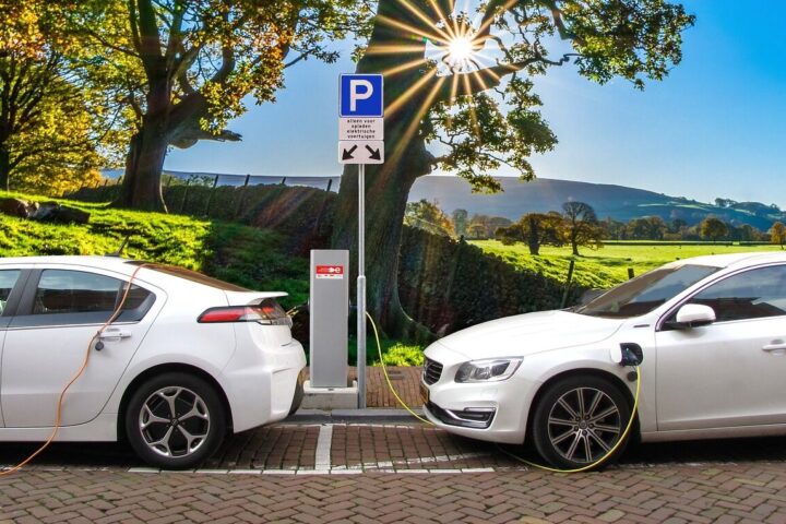 Representative image. Two white electric cars charge at a station under a bright sun and blue sky. Photo Source: Joenomias.