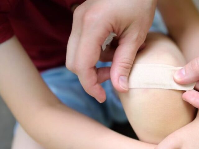 Representative Image. Mother hands applying antibacterial medical adhesive bandage on child's knee after falling down. First aid for kids after injury/trauma. Photo Source: SbytovaMN (IStock)