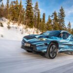 A car driving on a snowy road surrounded by a forest of tall evergreen trees. Photo Source - Mercedes Benz