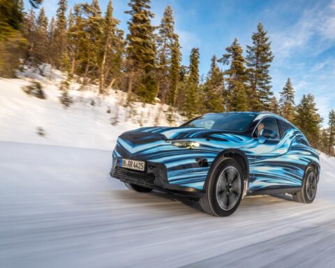 A car driving on a snowy road surrounded by a forest of tall evergreen trees. Photo Source - Mercedes Benz