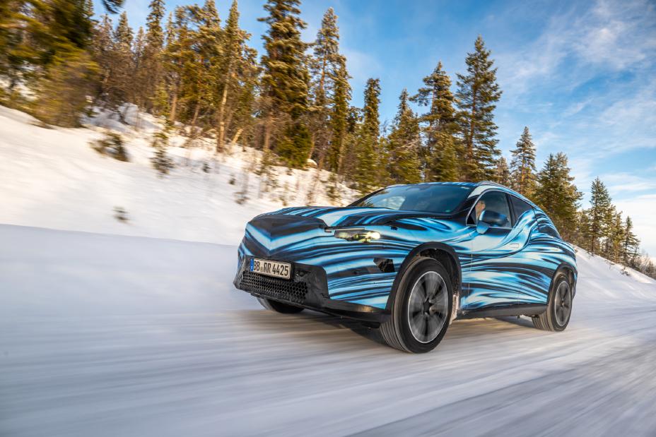 A car driving on a snowy road surrounded by a forest of tall evergreen trees. Photo Source - Mercedes Benz