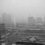 Representative Image: A cityscape covered in heavy smog, with high-rise buildings and construction cranes barely visible in the background. The scene suggests severe air pollution, likely due to industrial activities or coal dependency. Photo Source: Kevin Dooley (CC BY 2.0)