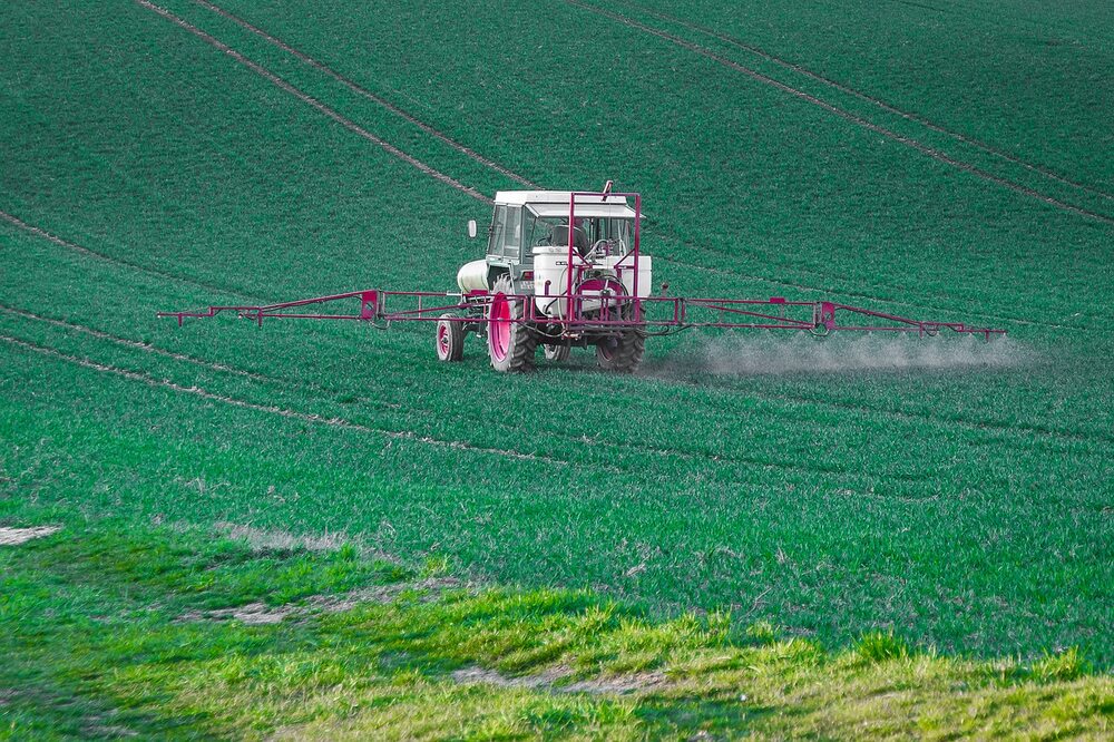 Representative Image: A tractor with a pesticide sprayer attached, working on a vast green agricultural field. The tractor is dispersing chemicals across the crops, likely for pest control, fertilization, or weed management. Photo source: needpic.com (maxmann (pixabay.com))