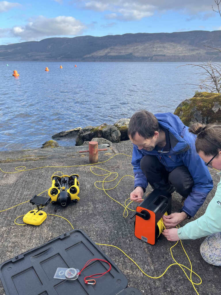 2 individuals engaged in a task involving a remotely operated underwater device. Photo Source - The Loch Ness Centre (Facebook)