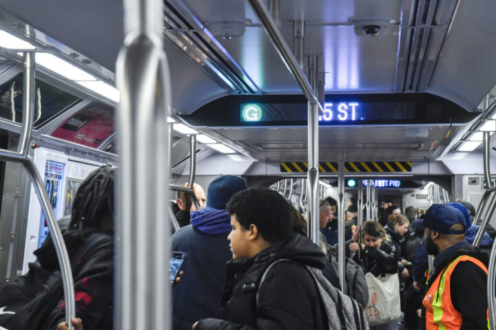 A crowded subway train with passengers standing and holding onto poles. The overhead digital sign displays "G" and "35 ST.", indicating that this is an MTA G Line train in New York City. Photo Source: MTA (https://www.mta.info/)