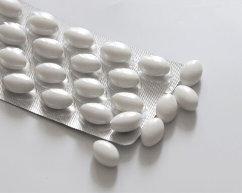 A blister pack containing white, oval-shaped pills, with some pills scattered on a white surface. Photo Source: Needpix.com- Olga1205 (pixabay.com)