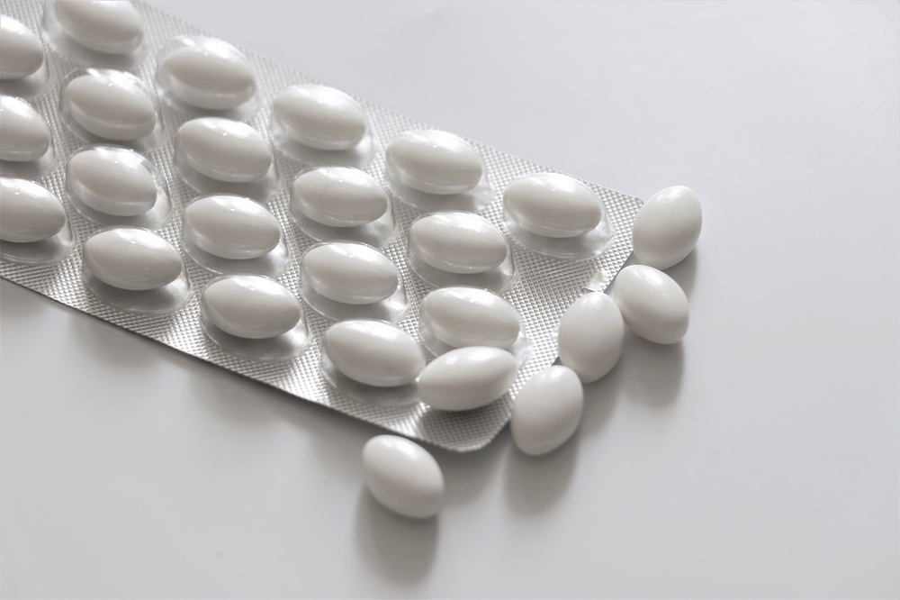 A blister pack containing white, oval-shaped pills, with some pills scattered on a white surface. Photo Source: Needpix.com- Olga1205 (pixabay.com)