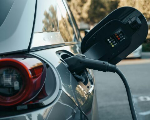 Representative Image: Electric vehicle (EV) being charged. The charging cable is plugged into the car’s charging port, with the port cover open, displaying indicator lights and symbols. Photo Source: Pexel (Kindel Media)