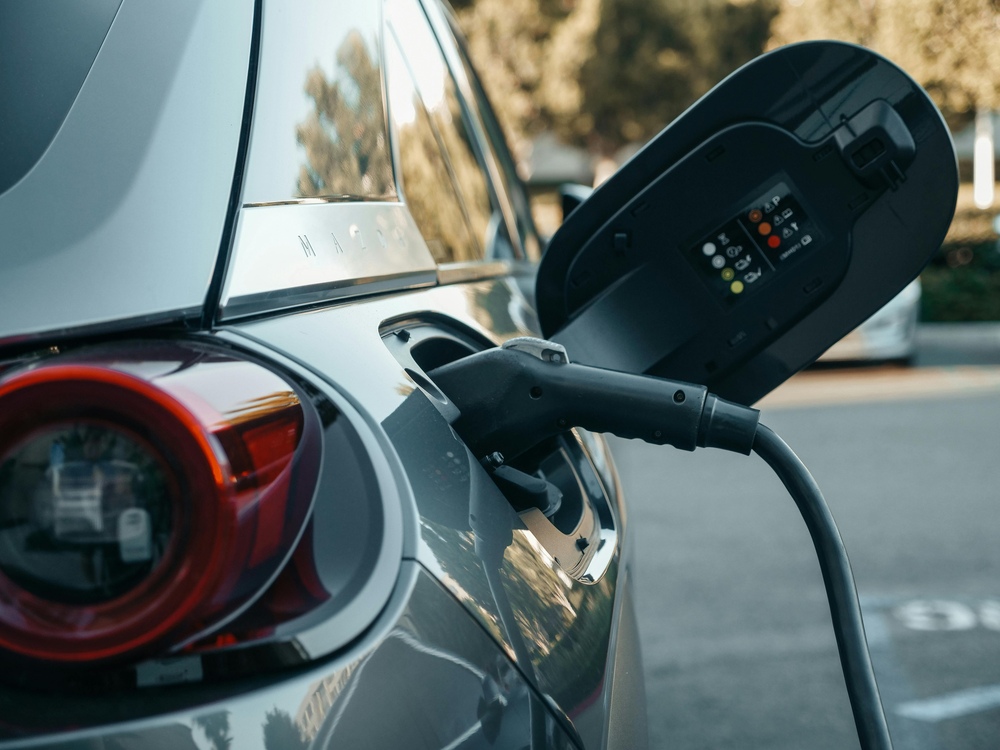 Representative Image: Electric vehicle (EV) being charged. The charging cable is plugged into the car’s charging port, with the port cover open, displaying indicator lights and symbols. Photo Source: Pexel (Kindel Media)