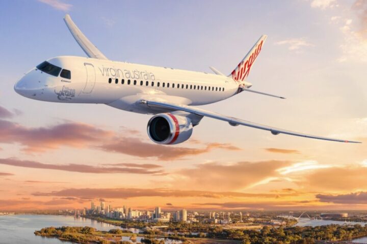 a Virgin Australia airplane gracefully flying over a vibrant cityscape during sunset. Photo Source - Virgin Australia