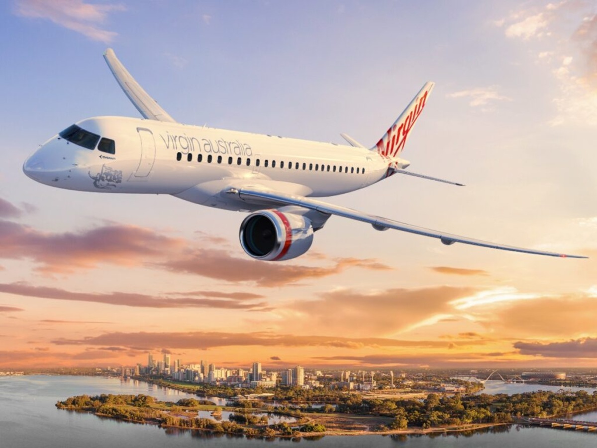 a Virgin Australia airplane gracefully flying over a vibrant cityscape during sunset. Photo Source - Virgin Australia